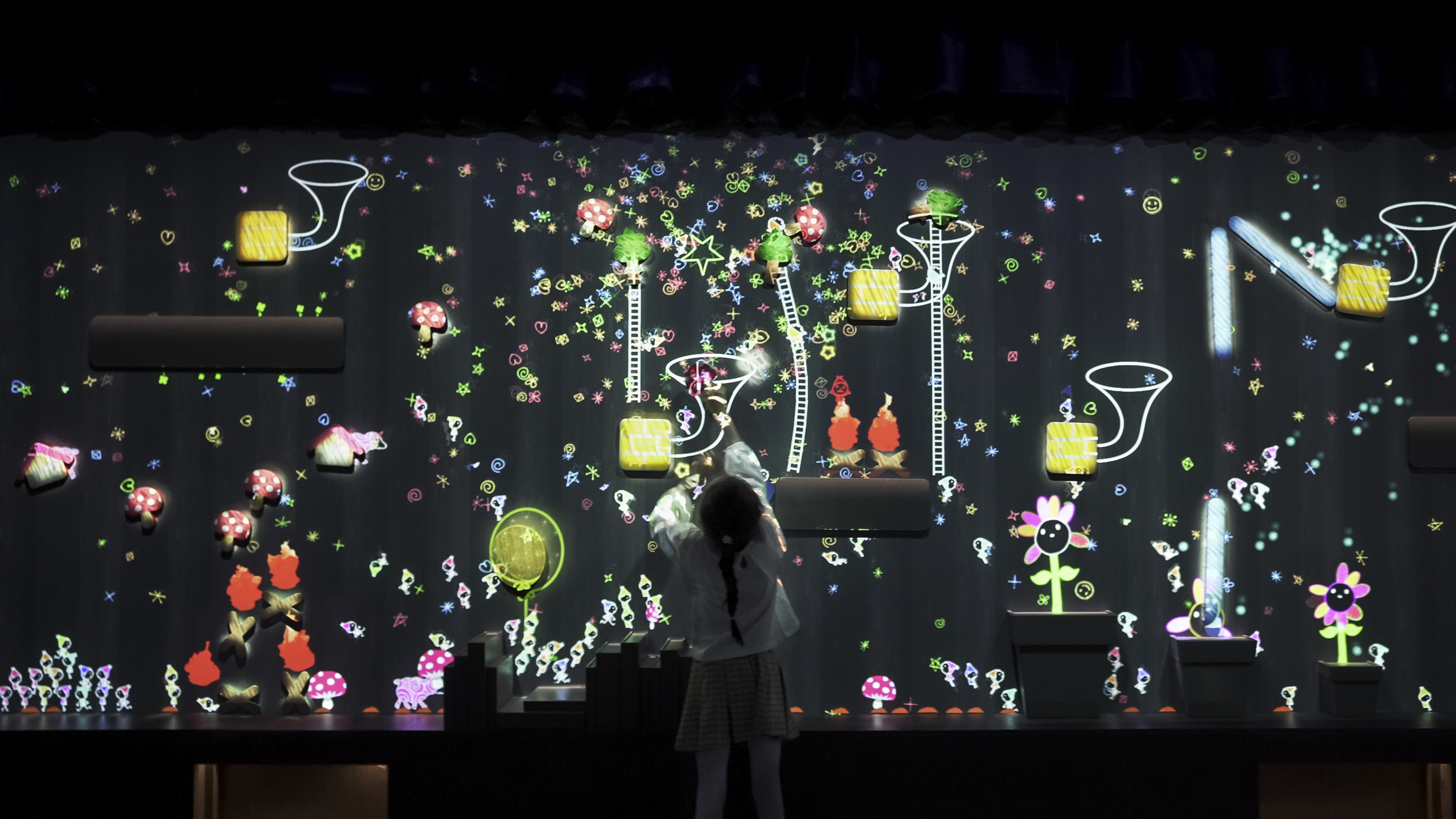 チームラボ、シンガポールの常設展「teamLab Future World」で、新たに3作品を公開。既存作品も複数リニューアル。のサブ画像2_ニコニコの種がスタンプに当たると、スタンプの種類によって、いろいろな音色を奏でる。チームラボ《こびとが住まう奏でる壁》© チームラボ